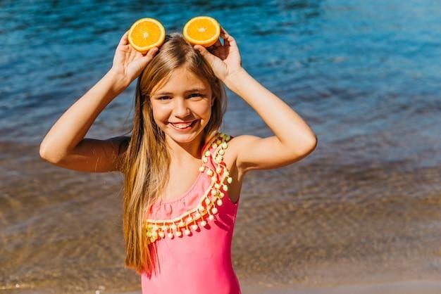 Девочка на берегу моря держит дольки апельсина как будто это уши